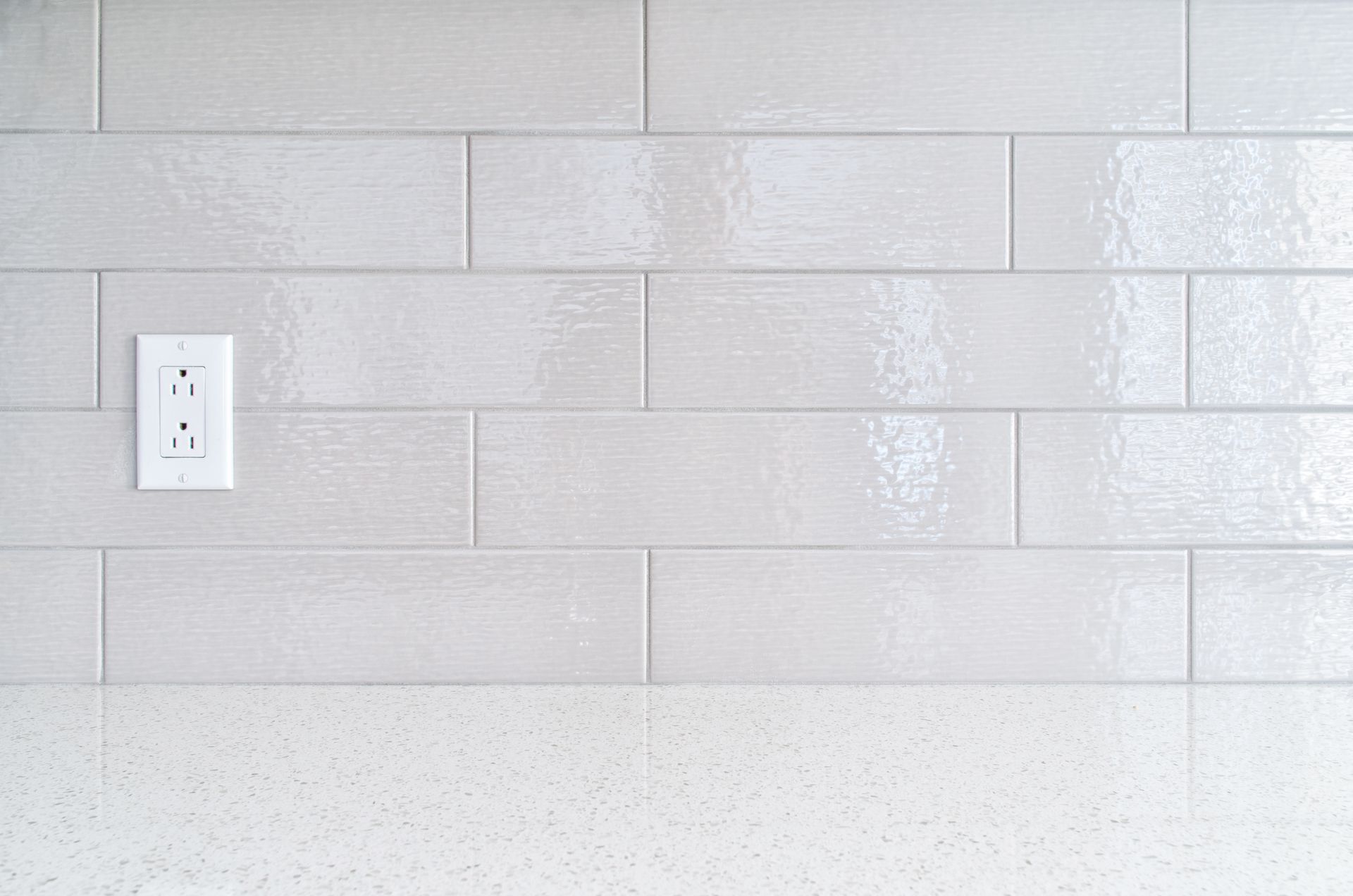 White tiled backsplash with electrical outlet above a countertop.
