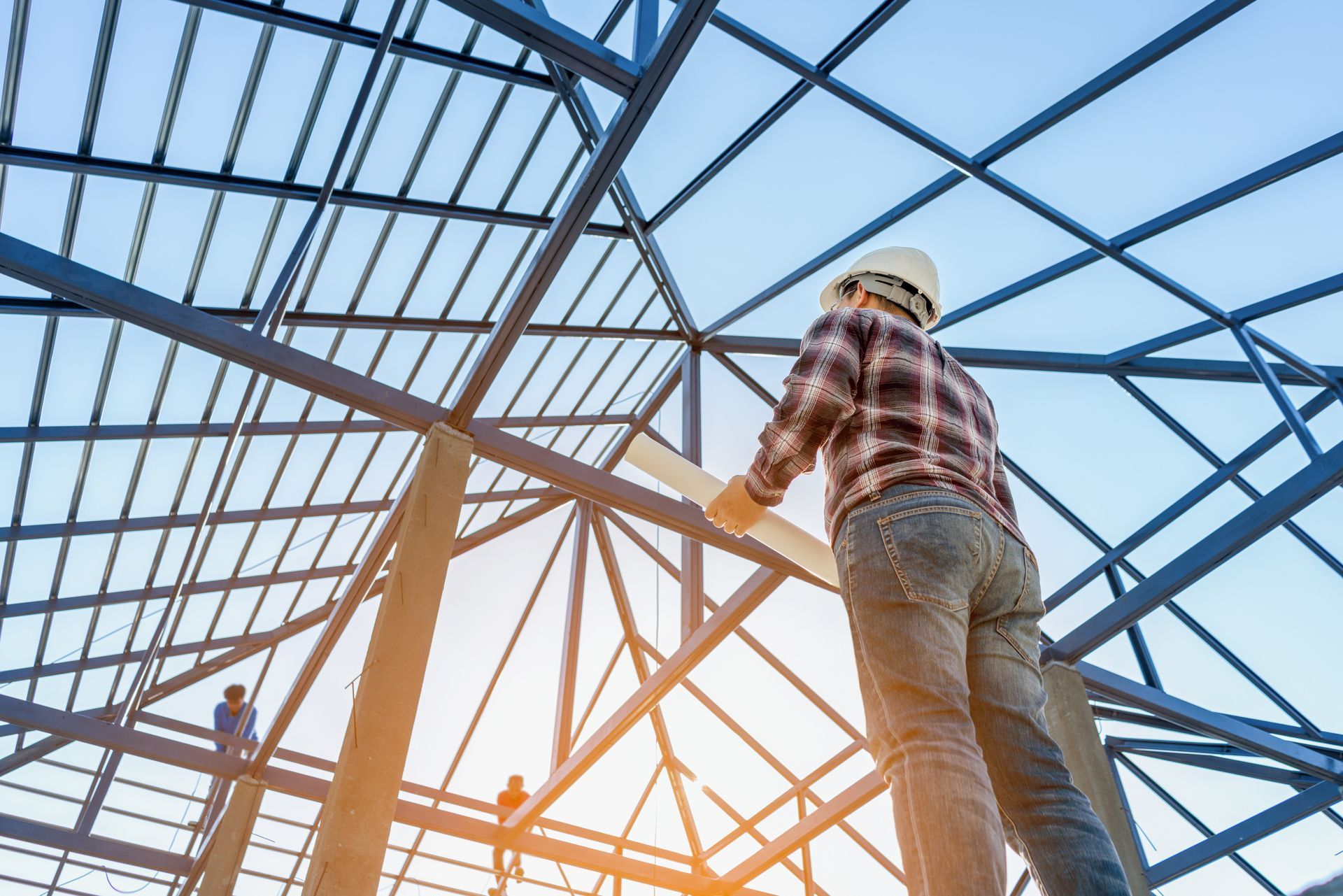 Construction worker in hard hat on steel beam framework at sunset.