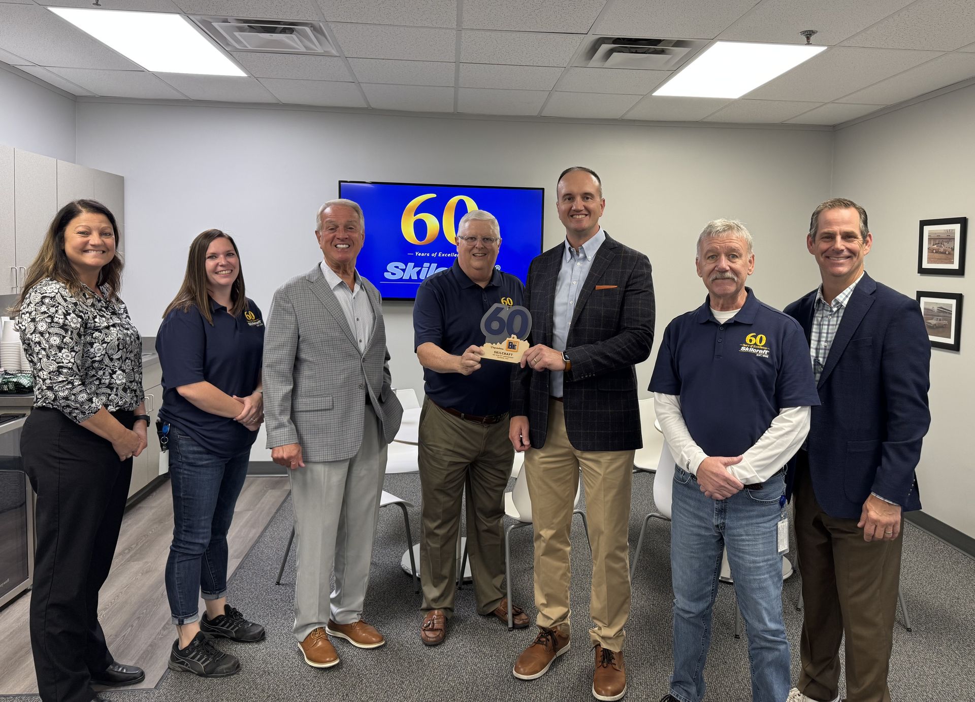 Group of people holding an award, celebrating in an office with a 60th anniversary banner.