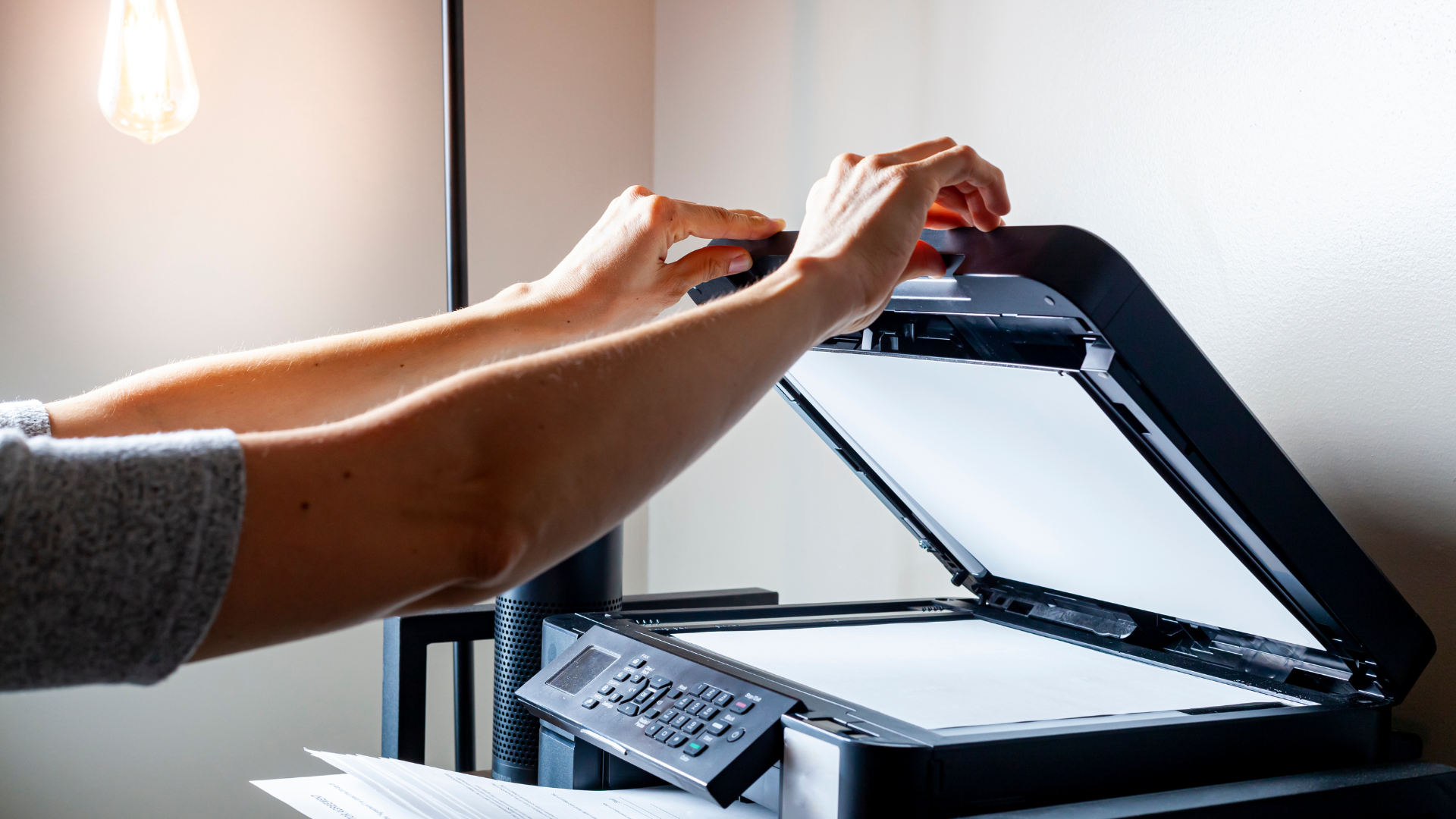Person opening a scanner lid in a home office setting, reaching with both hands.
