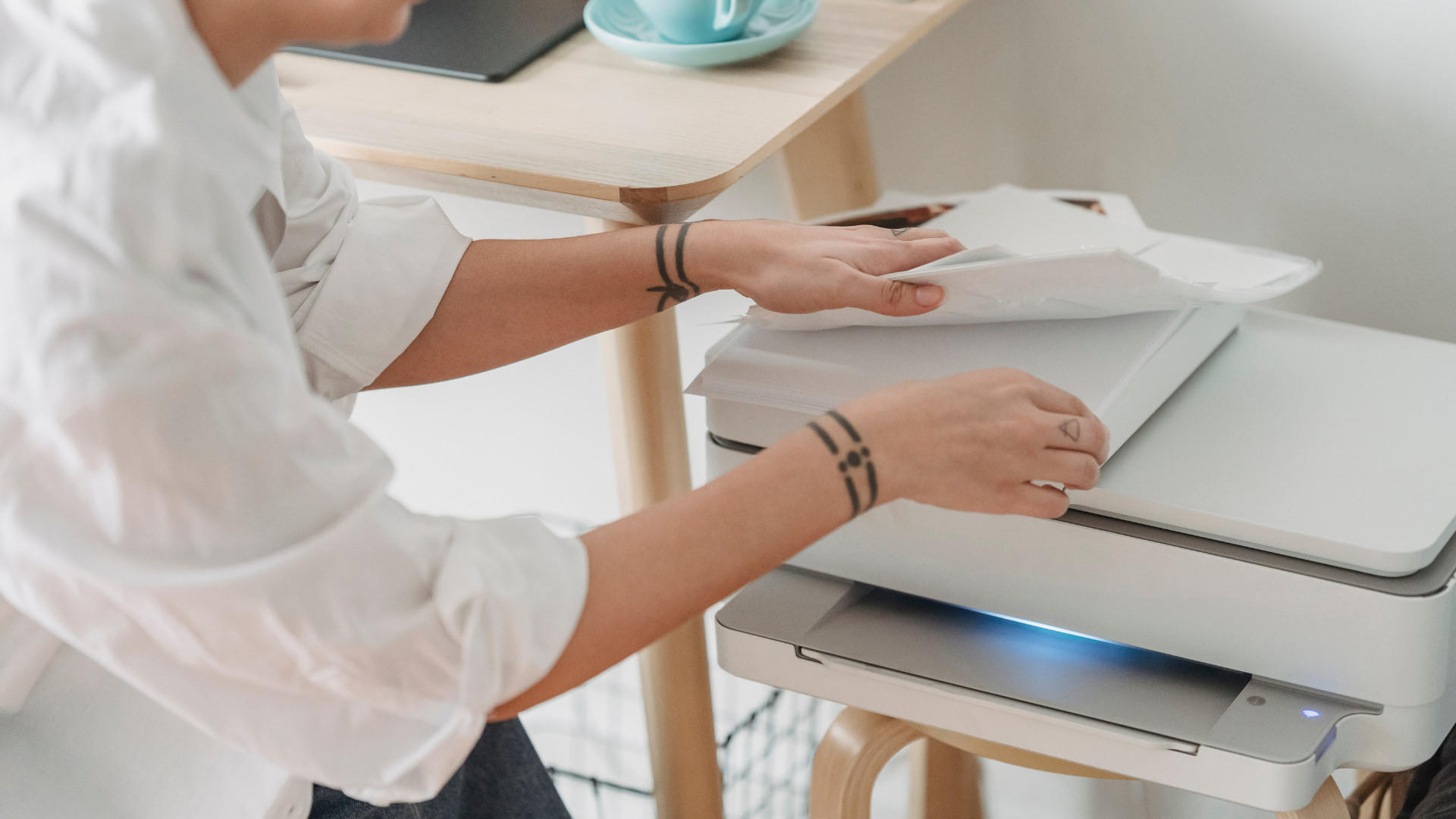Person in white shirt loading paper into a white printer on a desk.