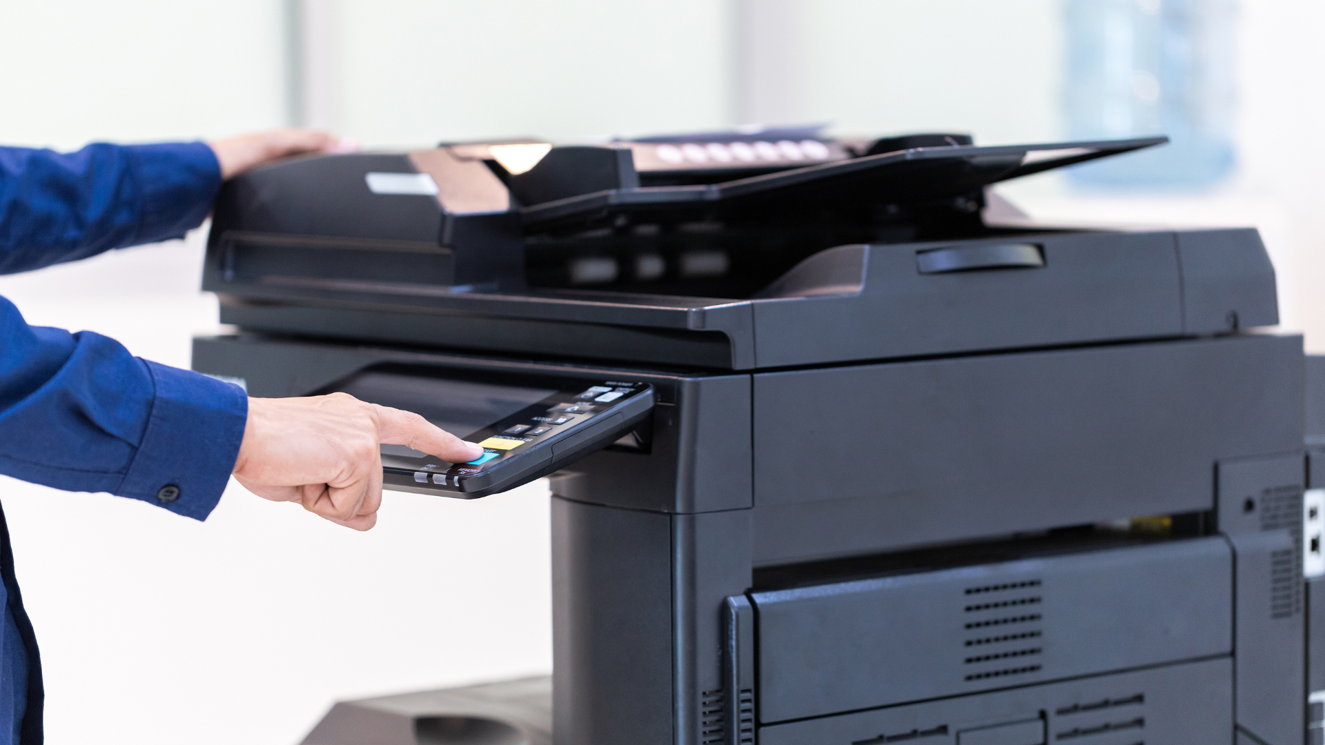 Person operating a black office copier. They press buttons on the control panel.