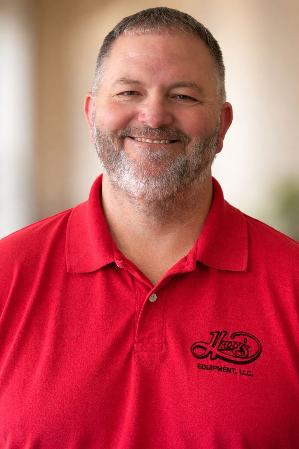 A smiling person wearing a bright red polo shirt with a black logo, standing against a blurred background.