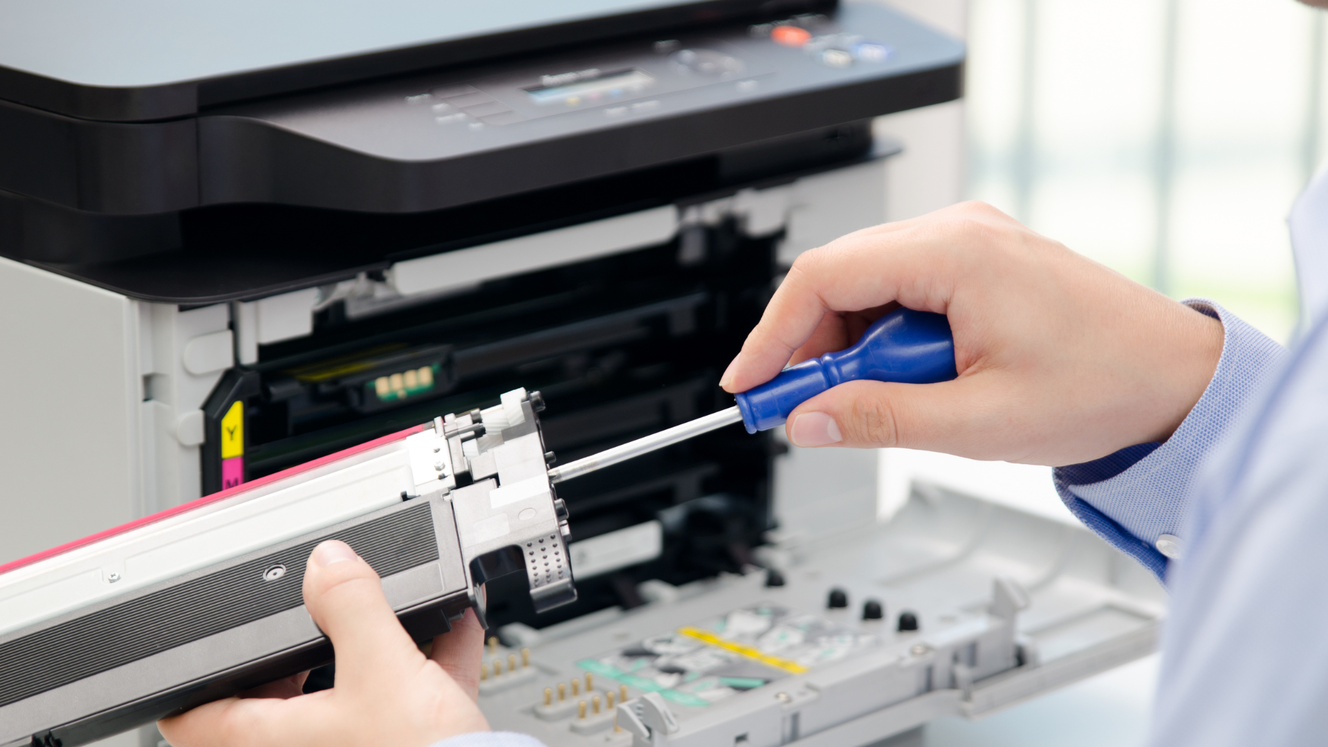 Person using a screwdriver to repair a color printer, removing a toner cartridge.
