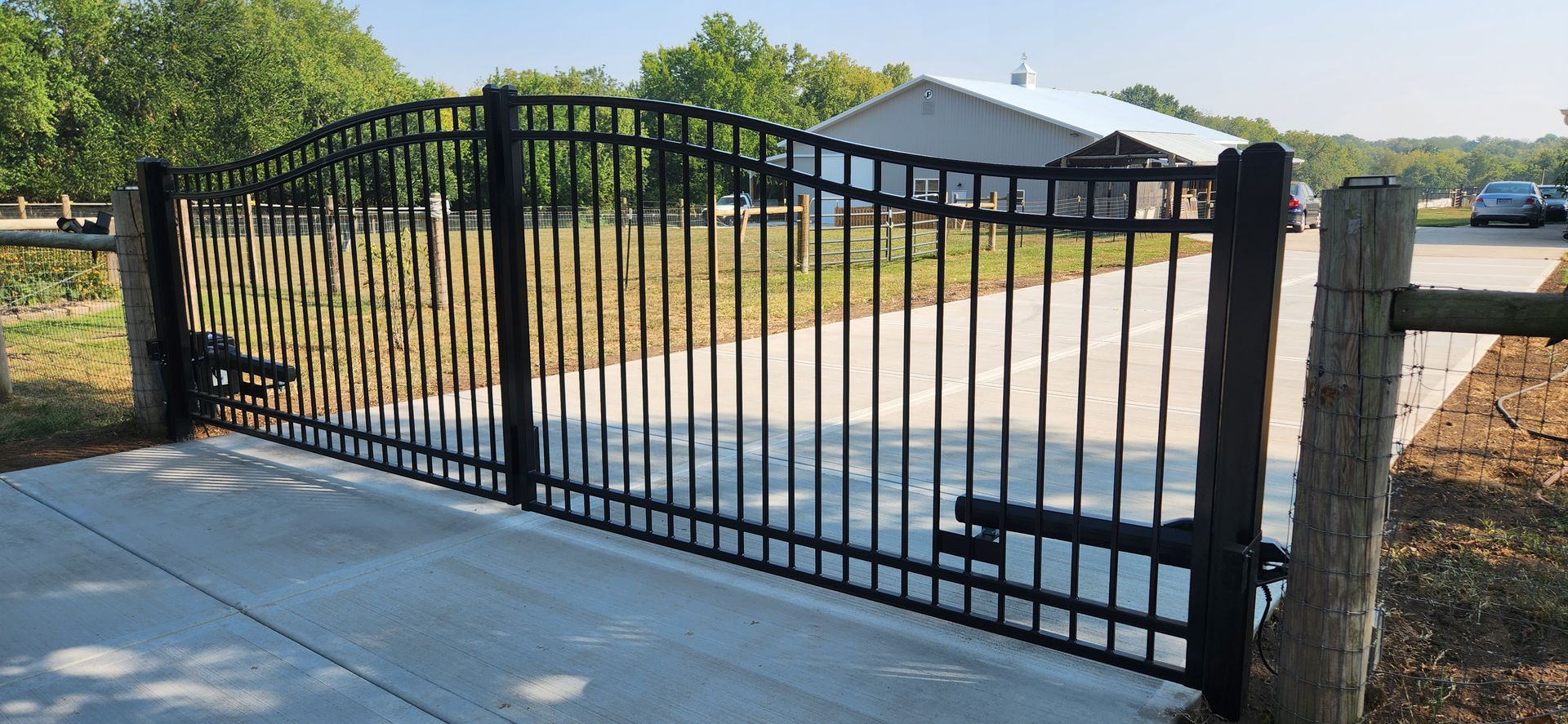 A black wrought iron gate is open to a driveway.