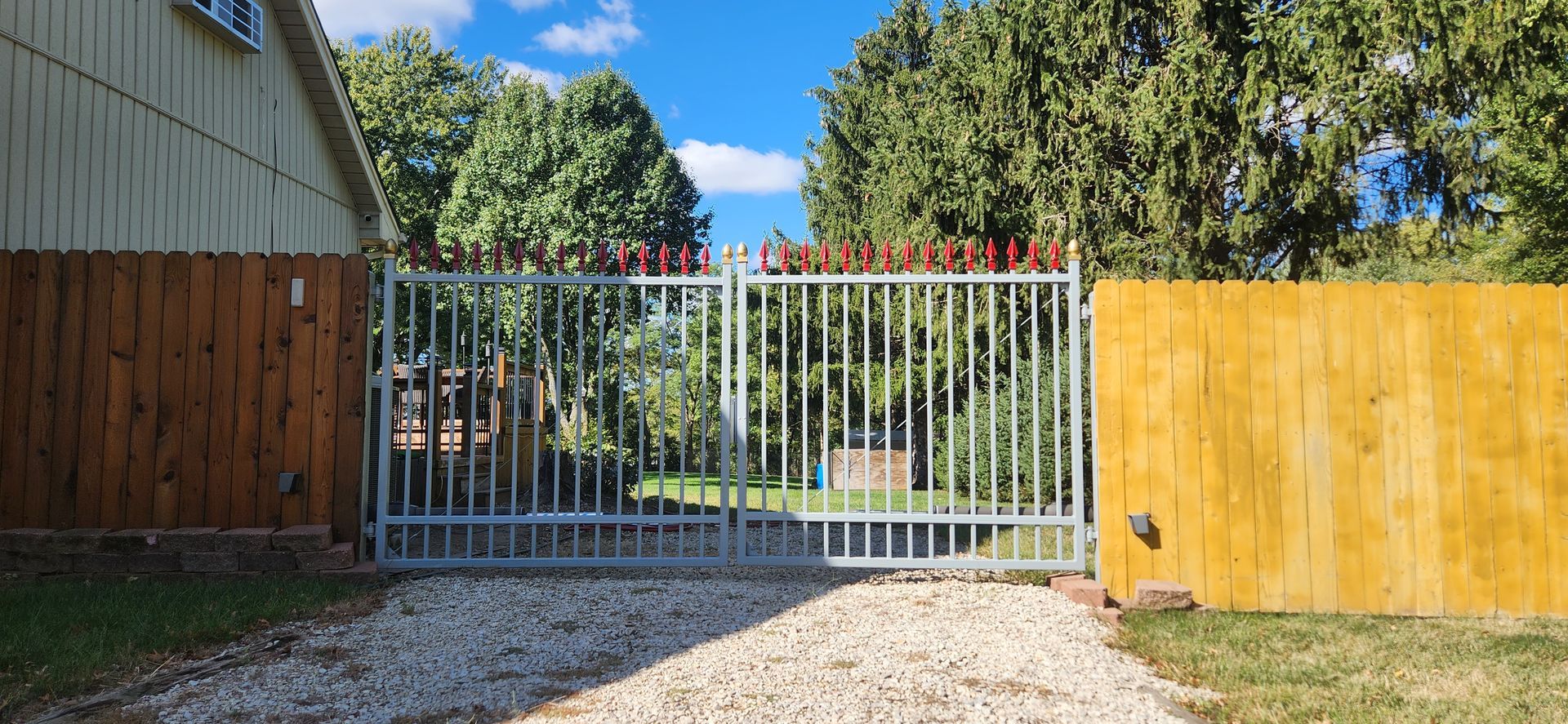 A driveway with a metal gate and a wooden fence.