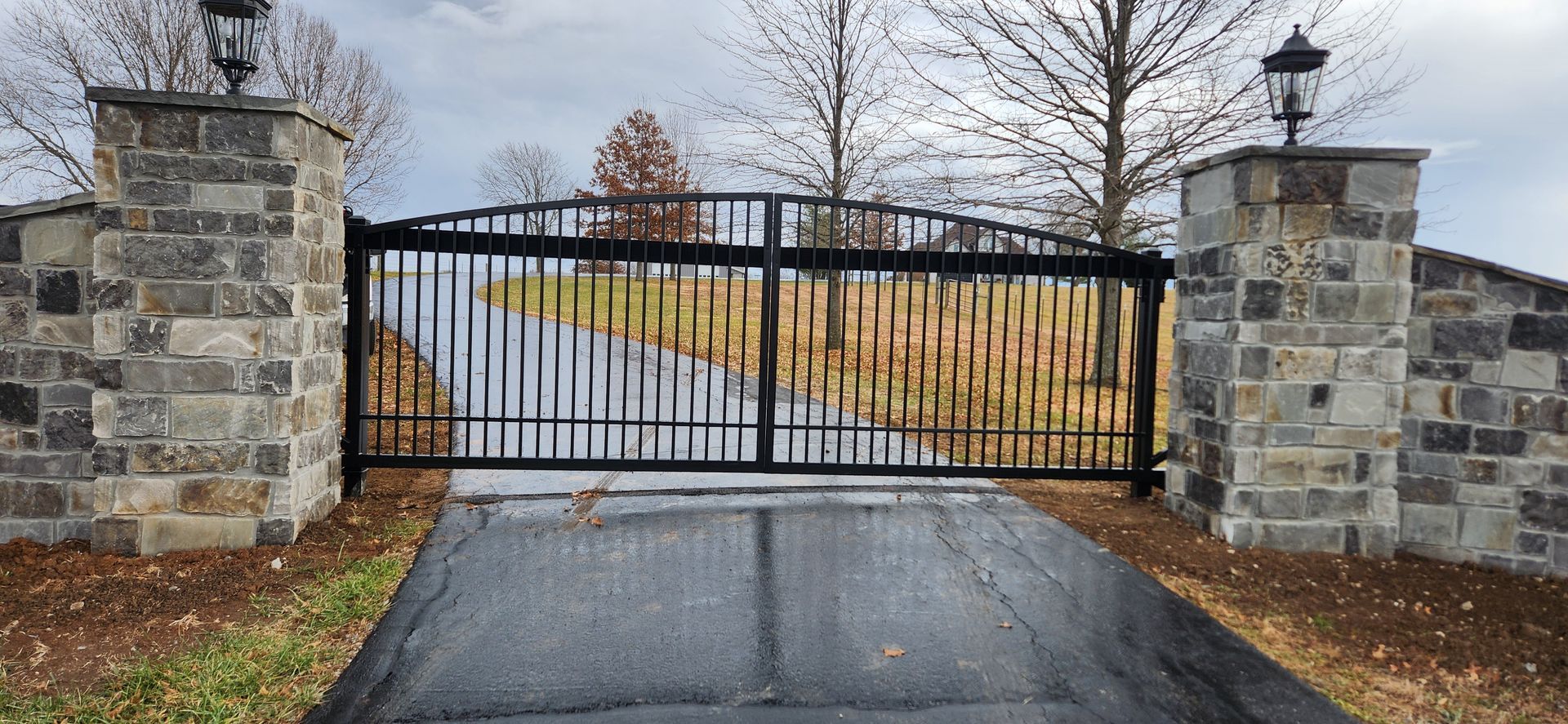 A black gate is sitting on the side of a road next to a stone wall.