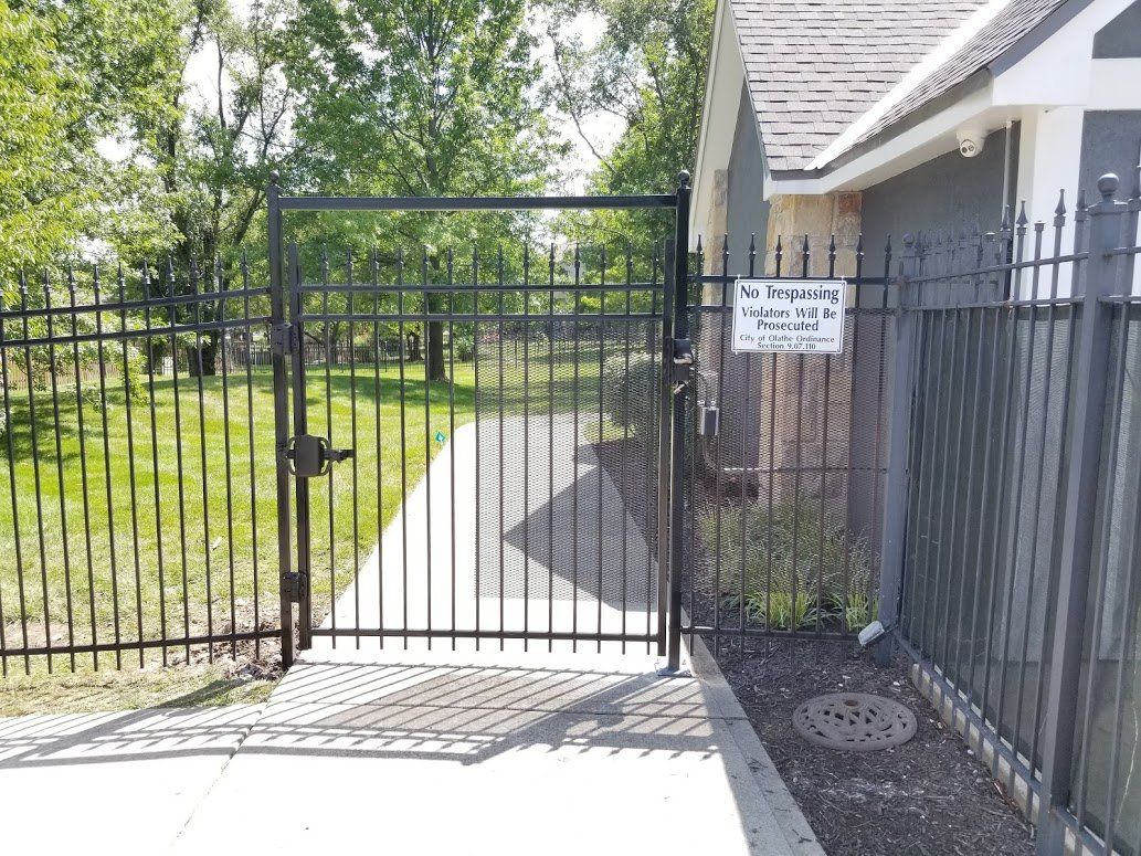 A black wrought iron gate is open to a driveway leading to a house.