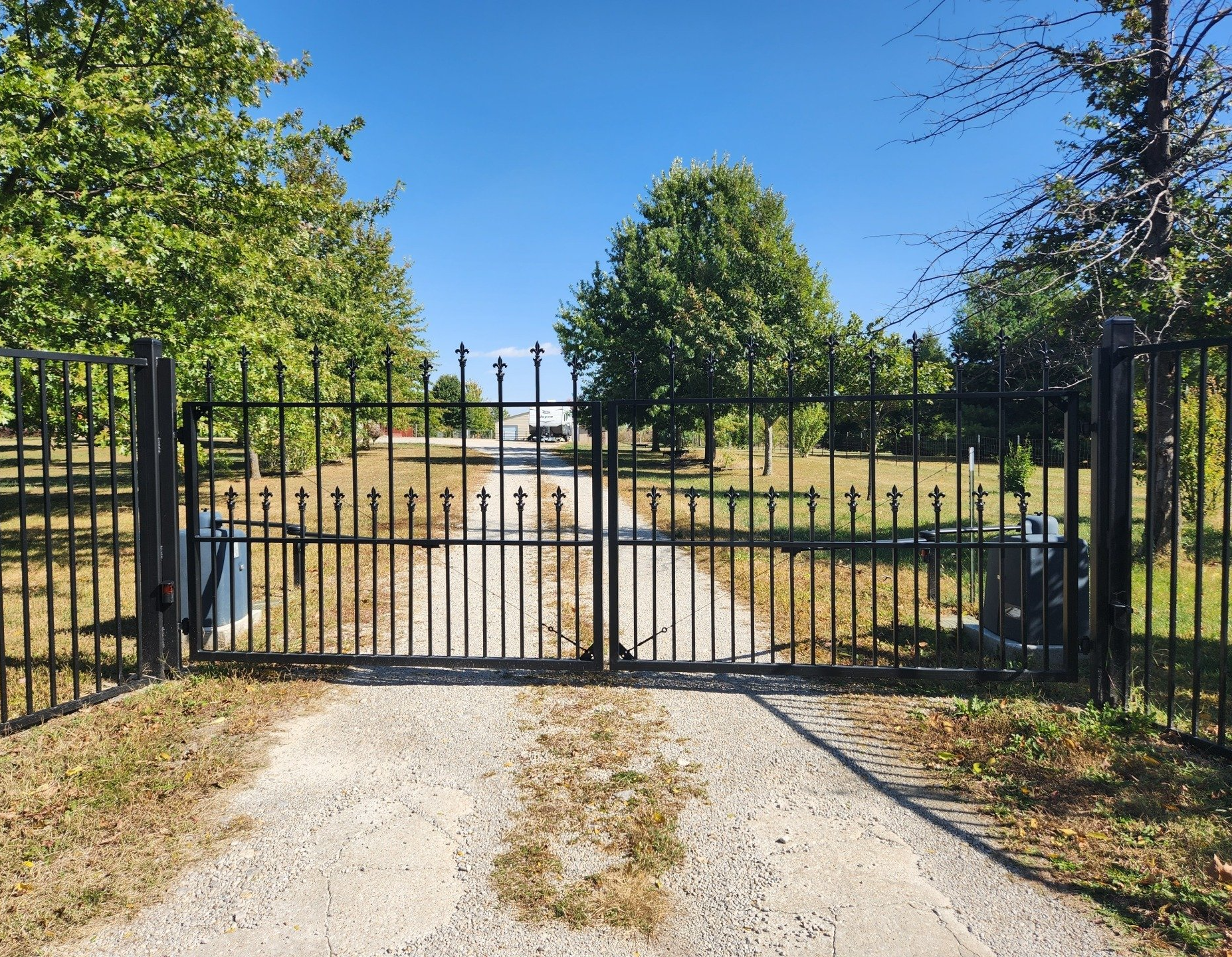 A wrought iron gate is closed on a gravel road.