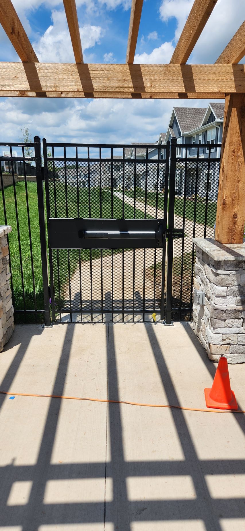A black metal gate is sitting under a wooden pergola.