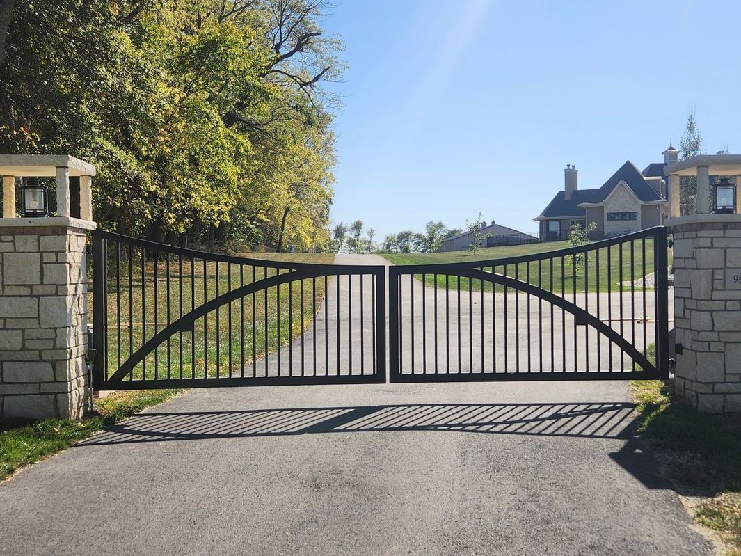A black gate is open to a driveway leading to a house.