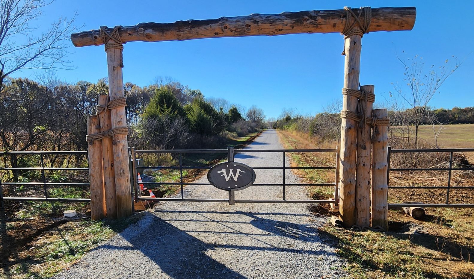 A wooden gate is leading to a dirt road.