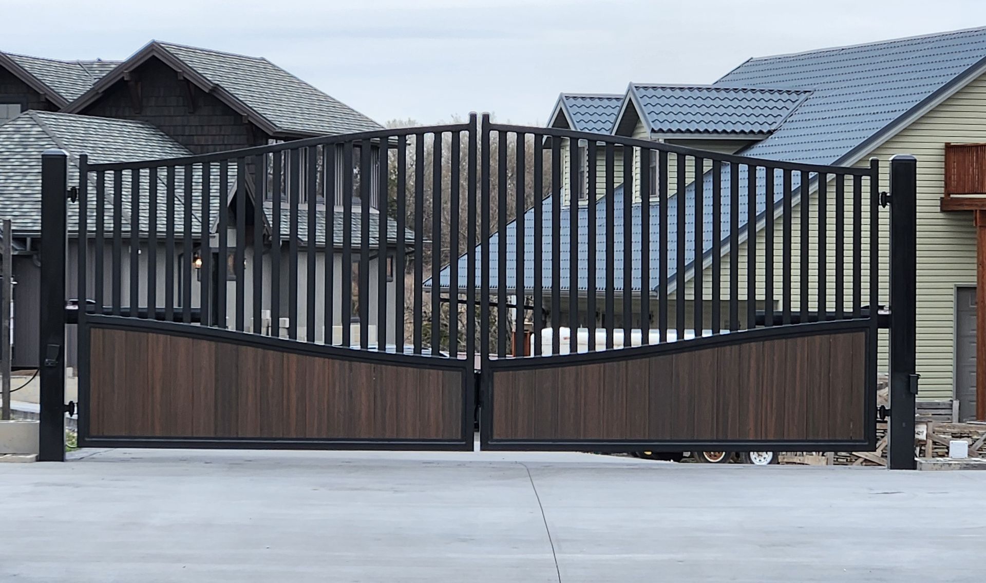 A black gate with a n on it is leading to a driveway.