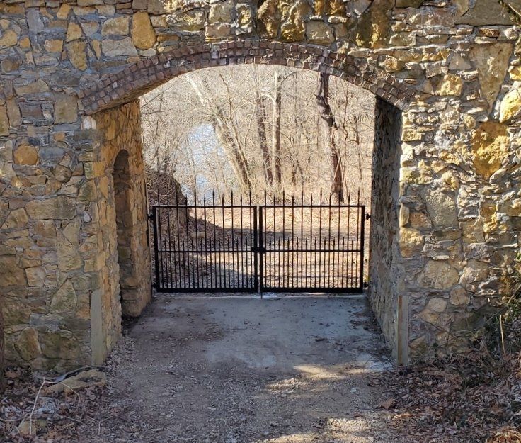 A stone archway with a wrought iron gate leading to a forest