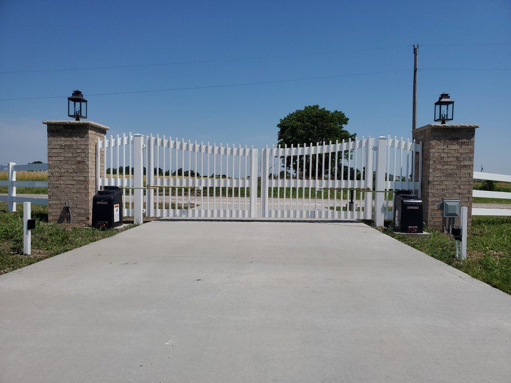 A concrete driveway with a white gate and a brick pillar.