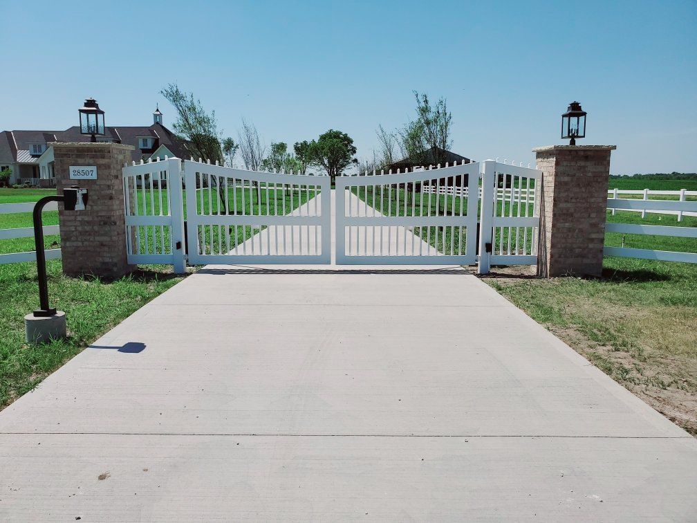 A concrete driveway with a white gate leading to a house