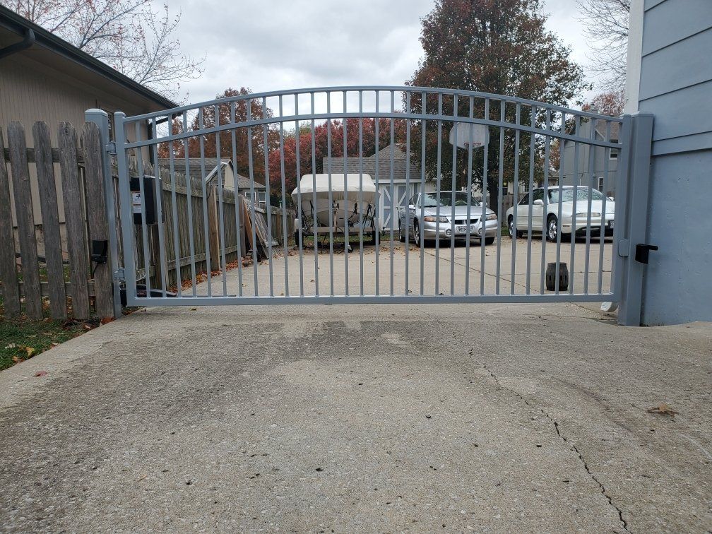 A metal gate is open to a driveway with cars parked behind it.