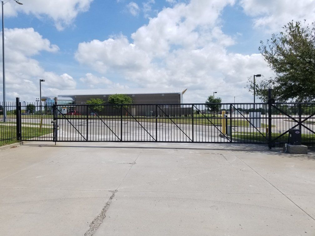 A sliding gate is open to a parking lot with a building in the background.