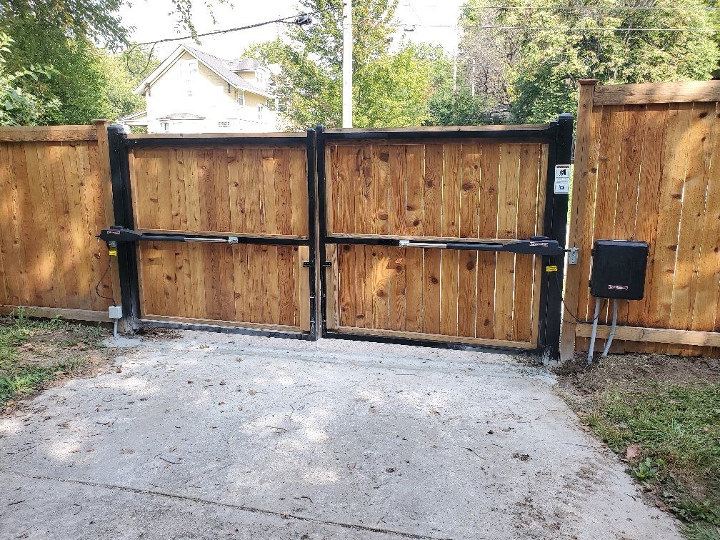 A wooden gate is open to a driveway next to a wooden fence.