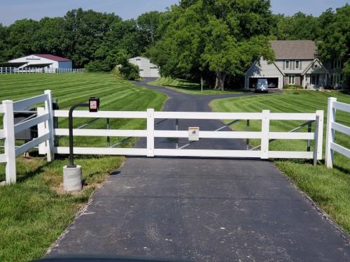 A white fence blocking a driveway to a house
