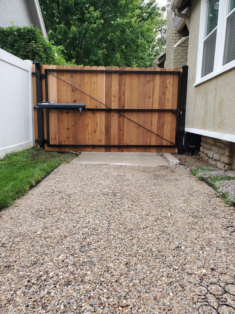 A wooden gate is sitting on the side of a gravel driveway next to a house.