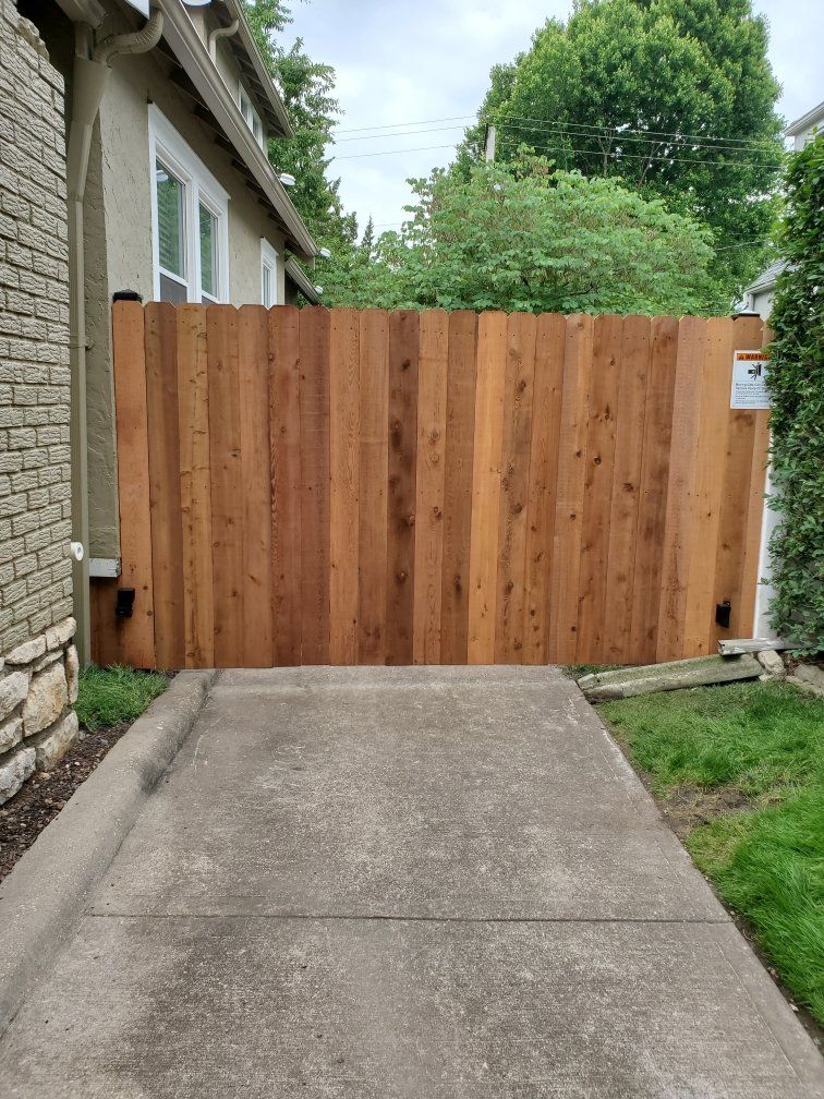 A wooden fence is sitting on the side of a driveway next to a house.