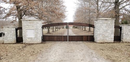 A large wooden gate is surrounded by stone pillars and trees.