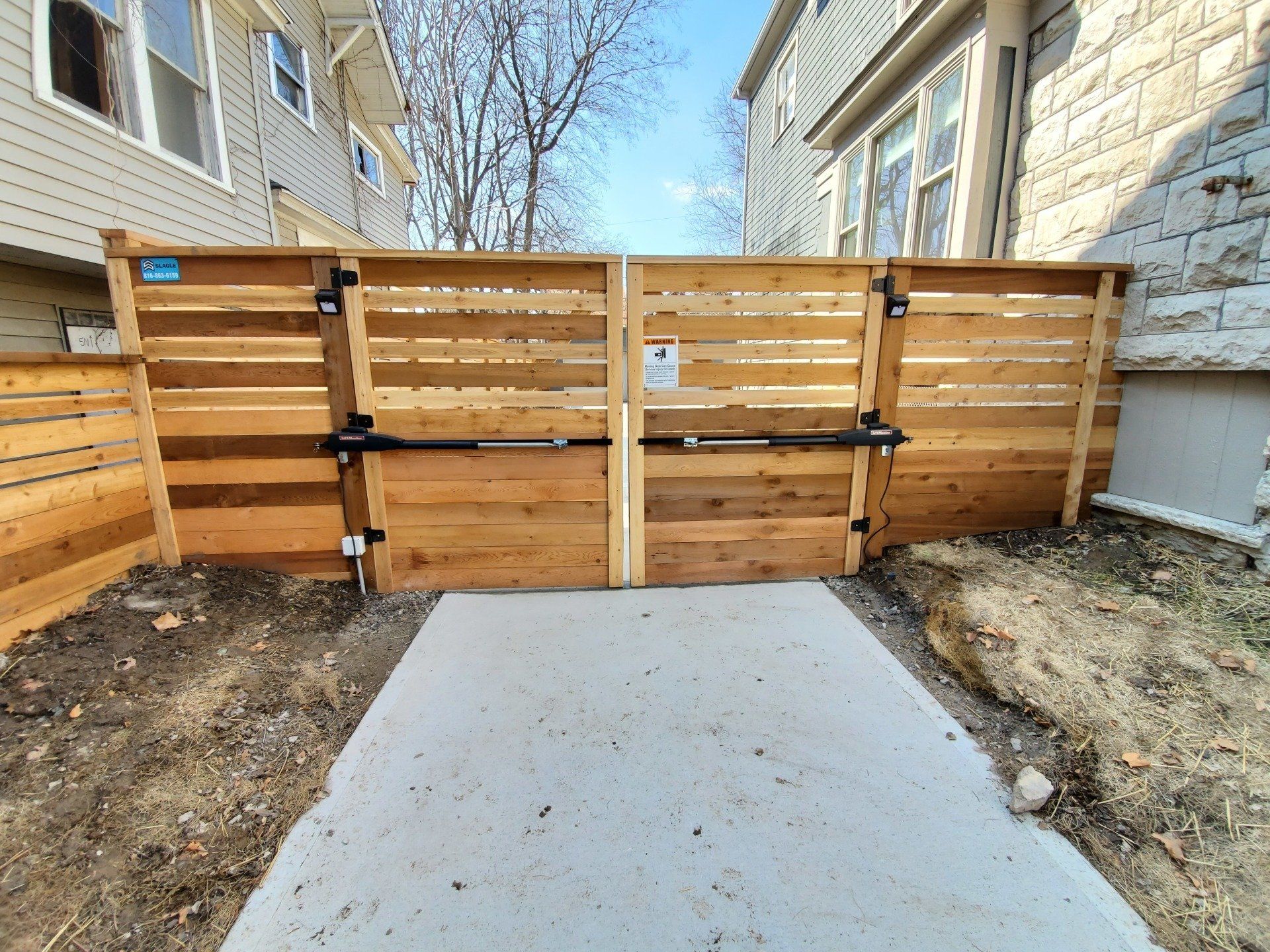 A wooden fence is surrounding a concrete walkway leading to a house.