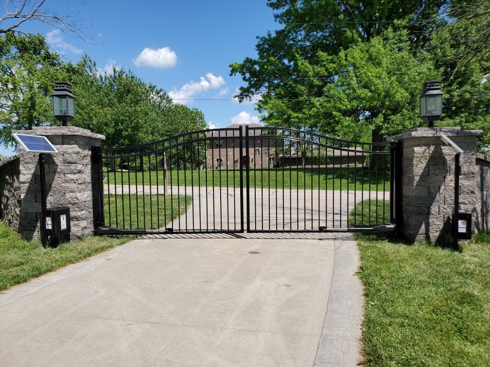 A large metal gate is open to a driveway leading to a house.