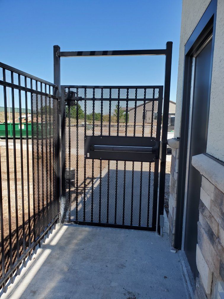 A black gate is sitting on the side of a building next to a fence.