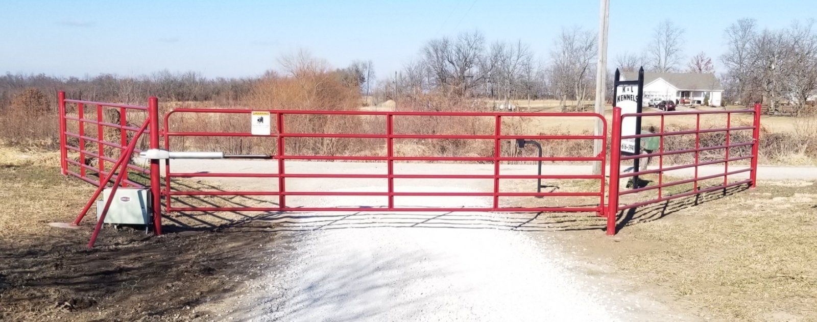 A red gate is sitting on the side of a dirt road.