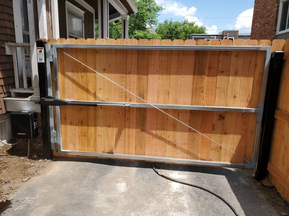 A wooden gate is open to a driveway next to a house.