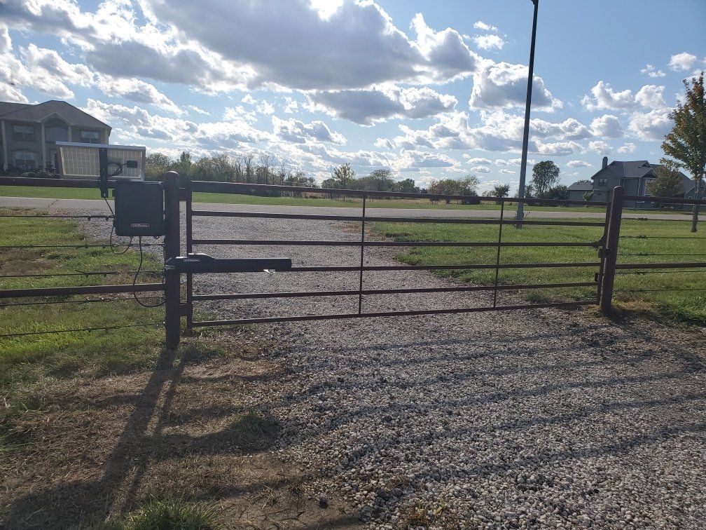 A metal gate is sitting in the middle of a gravel road.