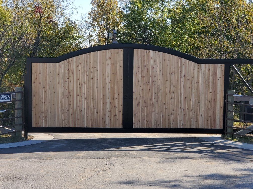 A wooden gate with a black frame is open to a driveway