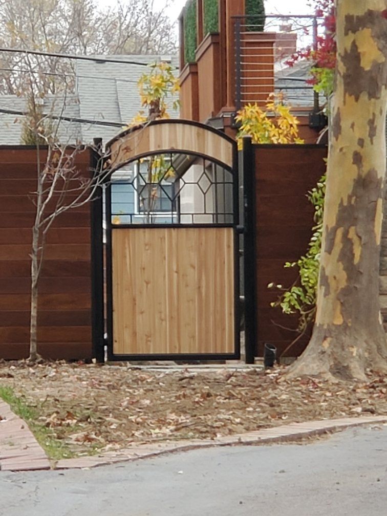 A wooden gate is surrounded by a fence and a tree
