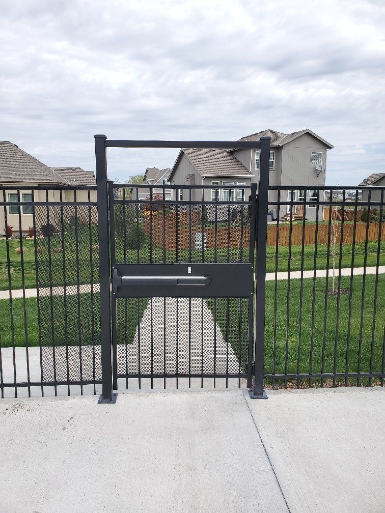 A black gate is sitting on the sidewalk next to a fence.