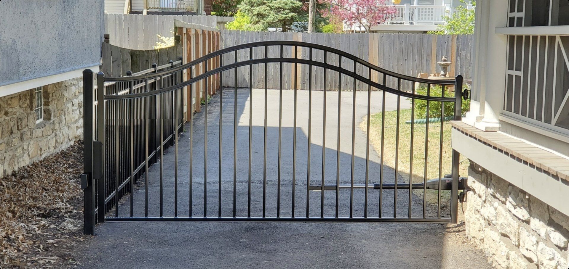 A black wrought iron gate is open to a driveway.