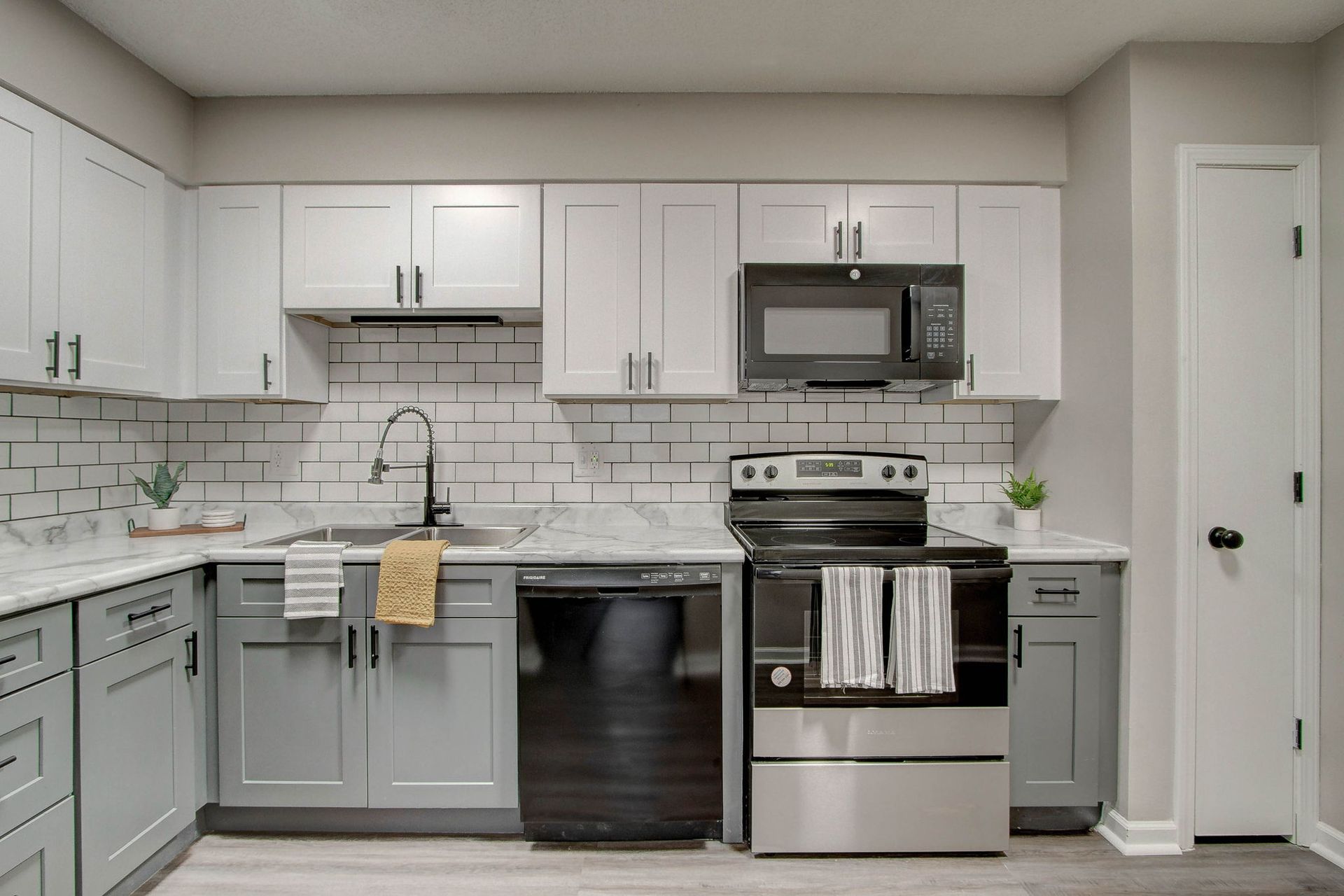 Modern kitchen with white and gray cabinets, black appliances, and subway tile backsplash.