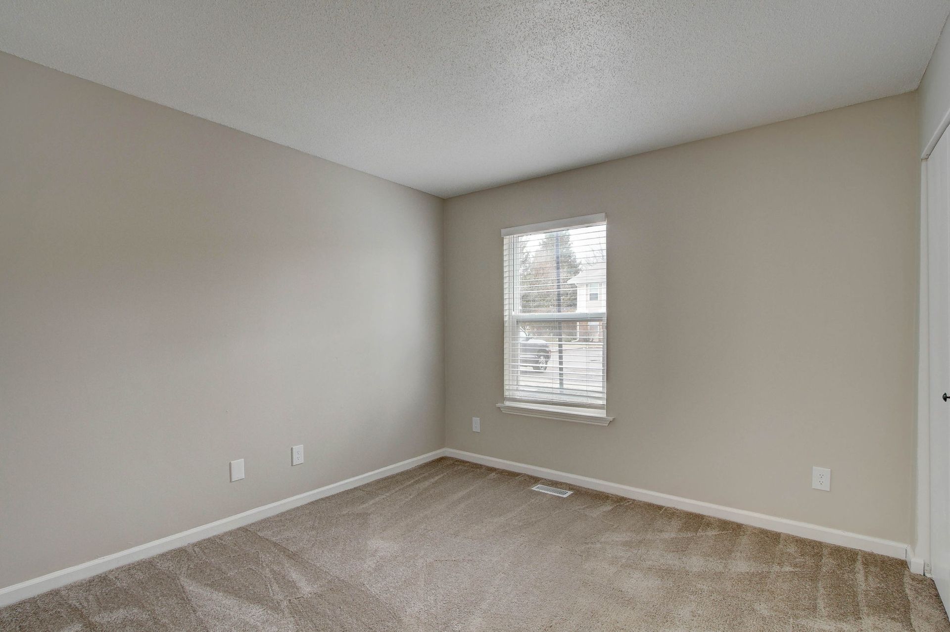 Empty room with beige walls, carpet, and a small window with blinds.