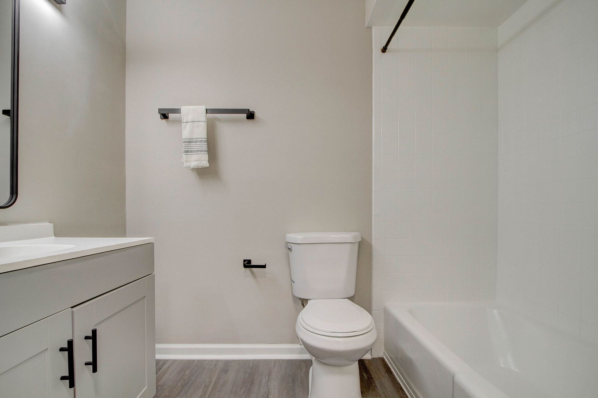 Bathroom with white toilet, tub, vanity, black fixtures, gray walls and flooring.