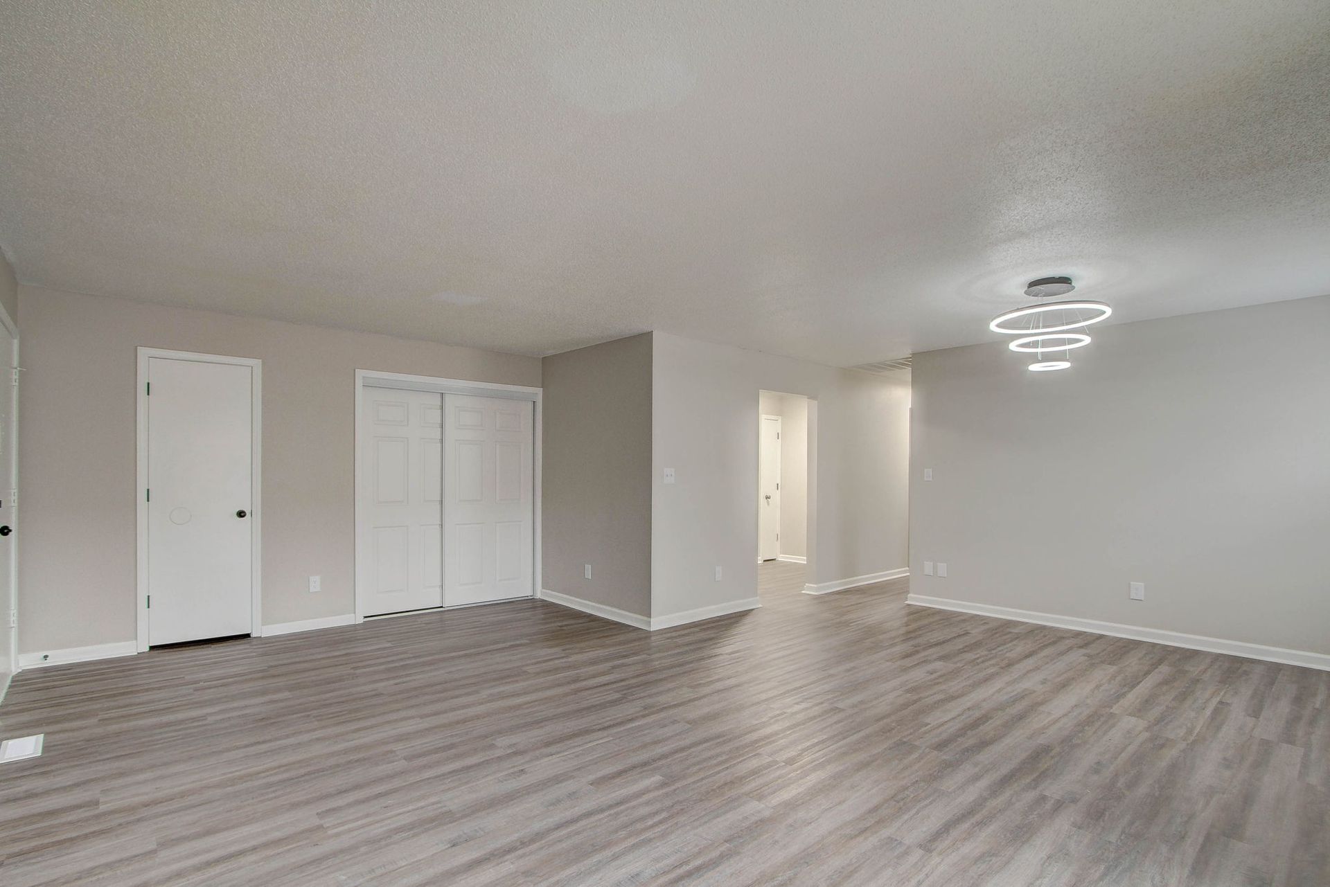 Empty living room with gray walls, light wood-look floors, and a modern chandelier.