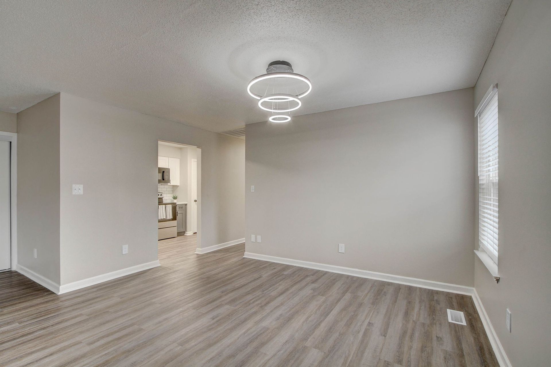 Empty living room with gray walls, wood-look floors, and a modern pendant light fixture.