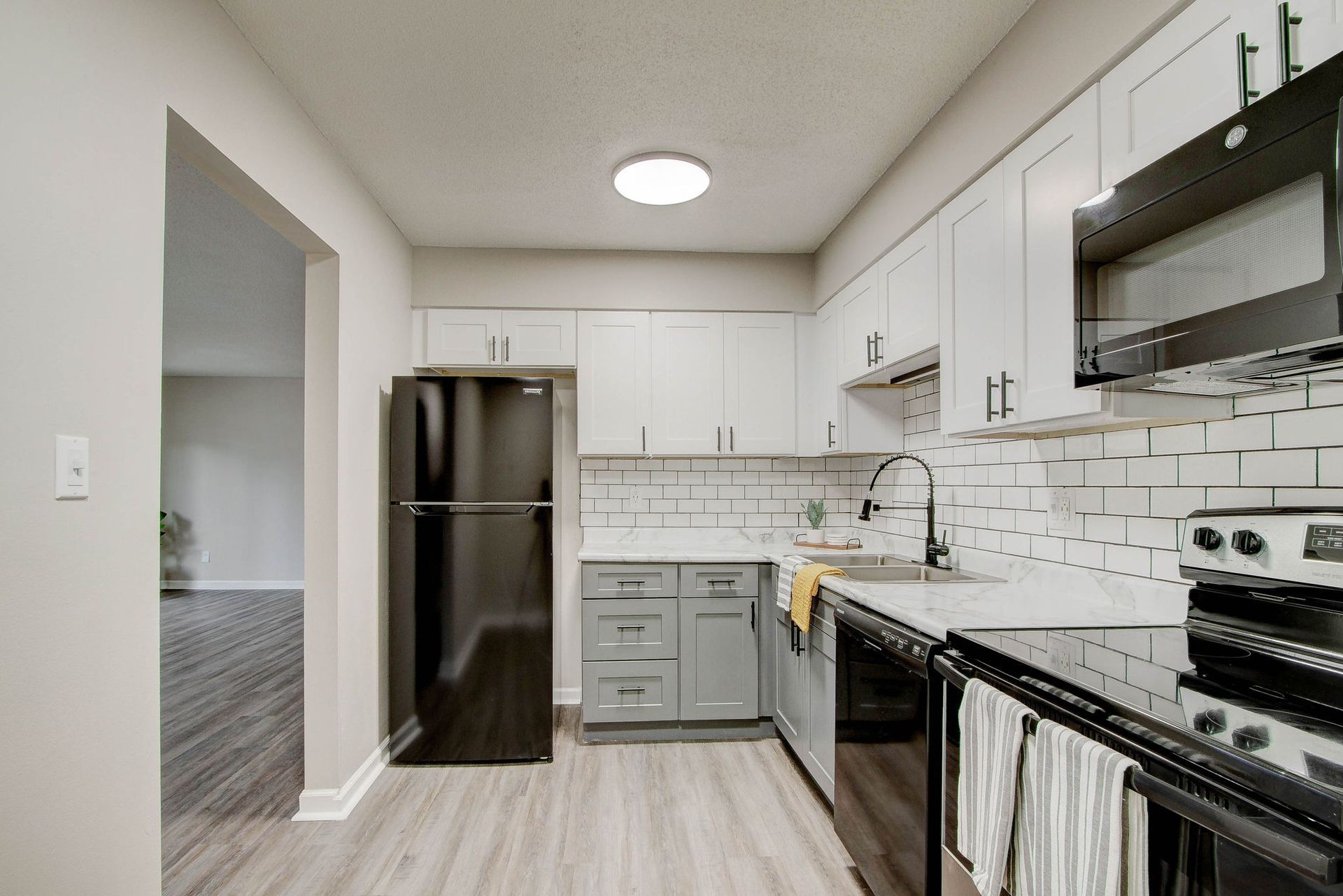 Modern kitchen with white and gray cabinets, black appliances, and light gray floors.