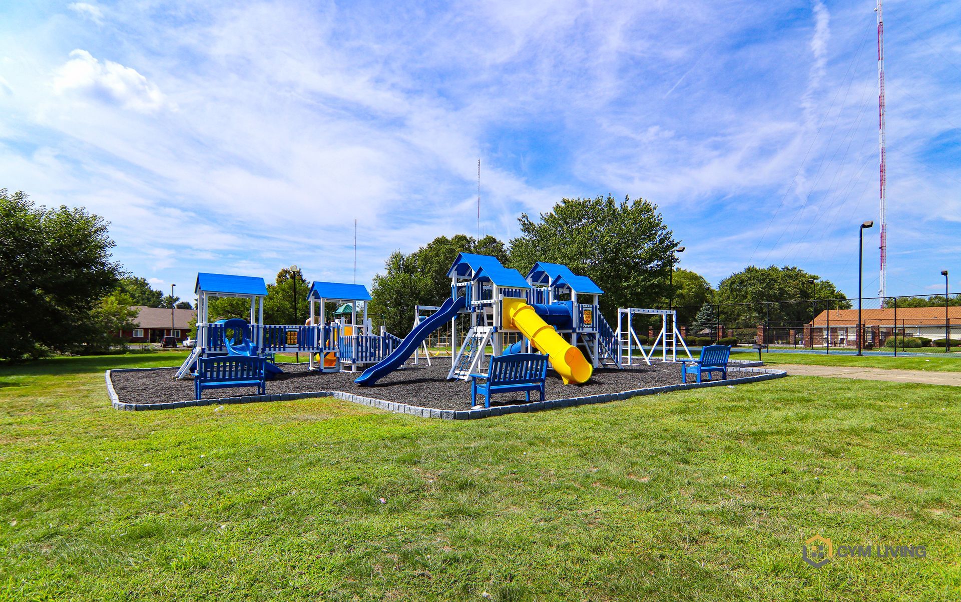 Playground equipment on a grassy area, with blue and yellow slides, swings, and towers. Overcast day.