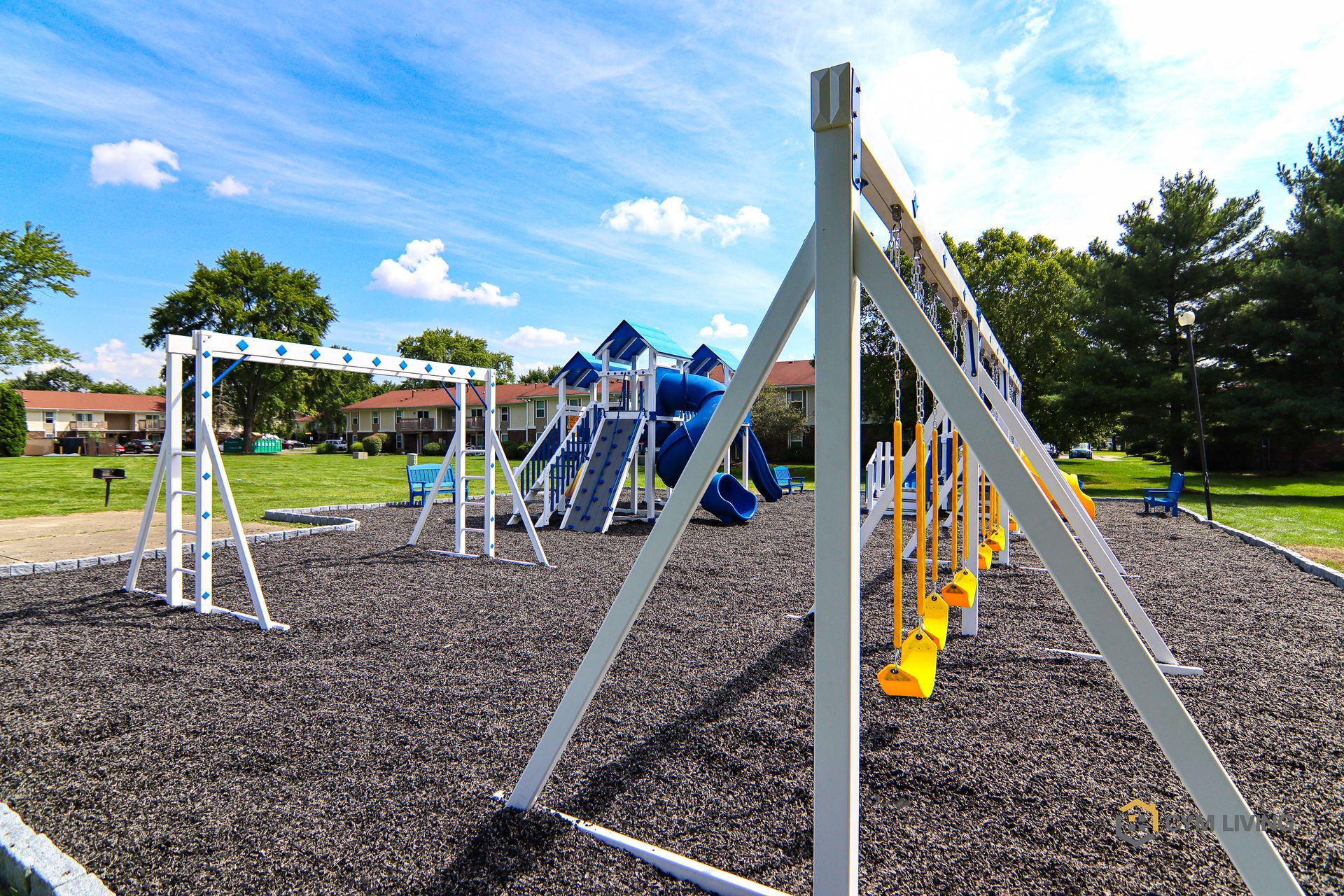 Playground with swings and slides under a blue sky; mulch ground.