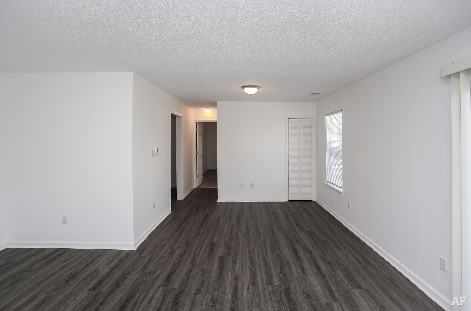 Empty living room with gray flooring, white walls, and a hallway.