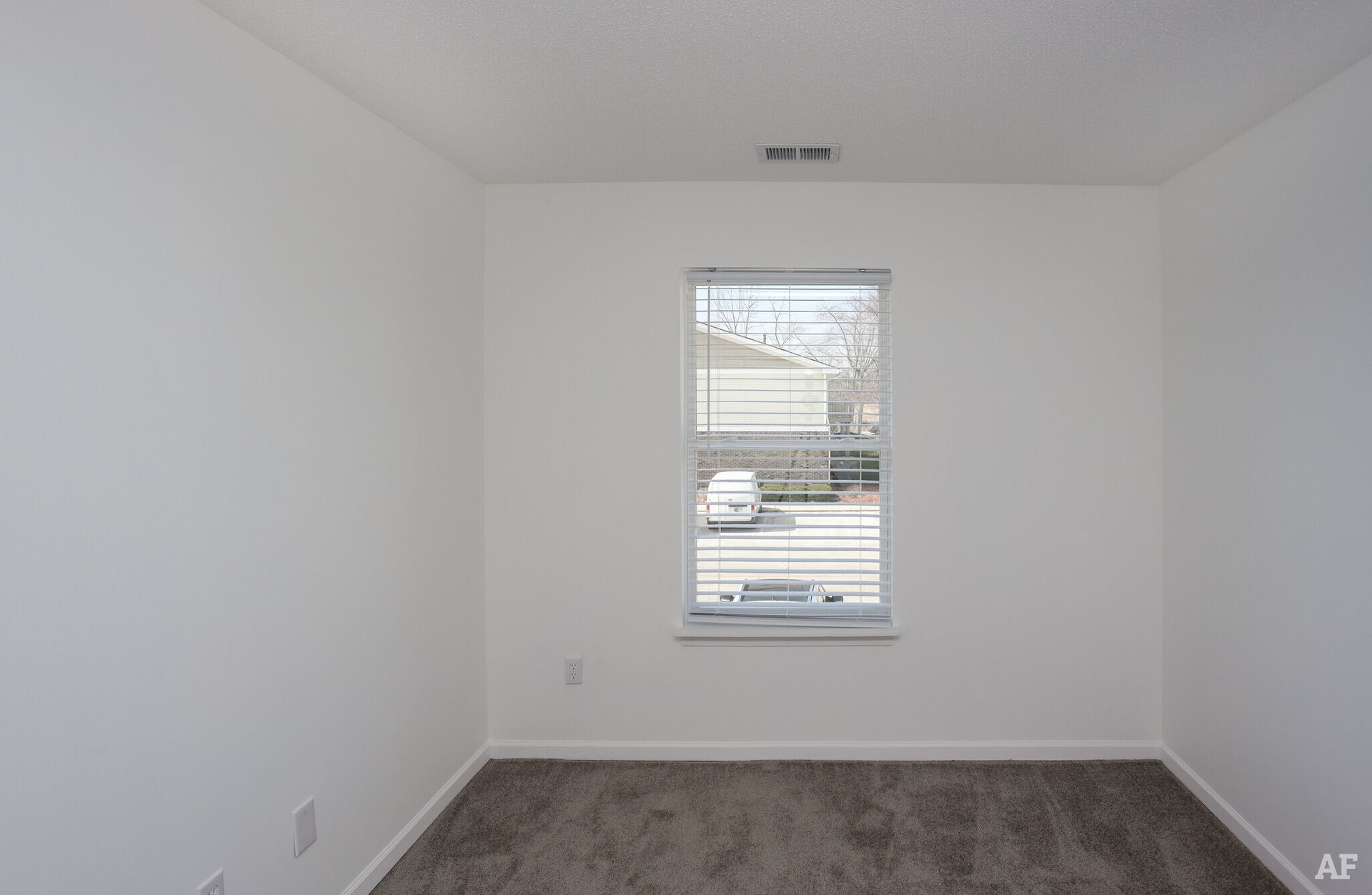 Empty room with a window and blinds, white walls, and gray carpet.