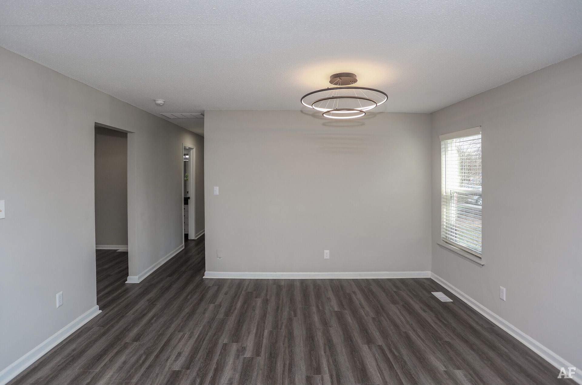 Empty dining room with gray walls, wood-look floor, and a modern light fixture.