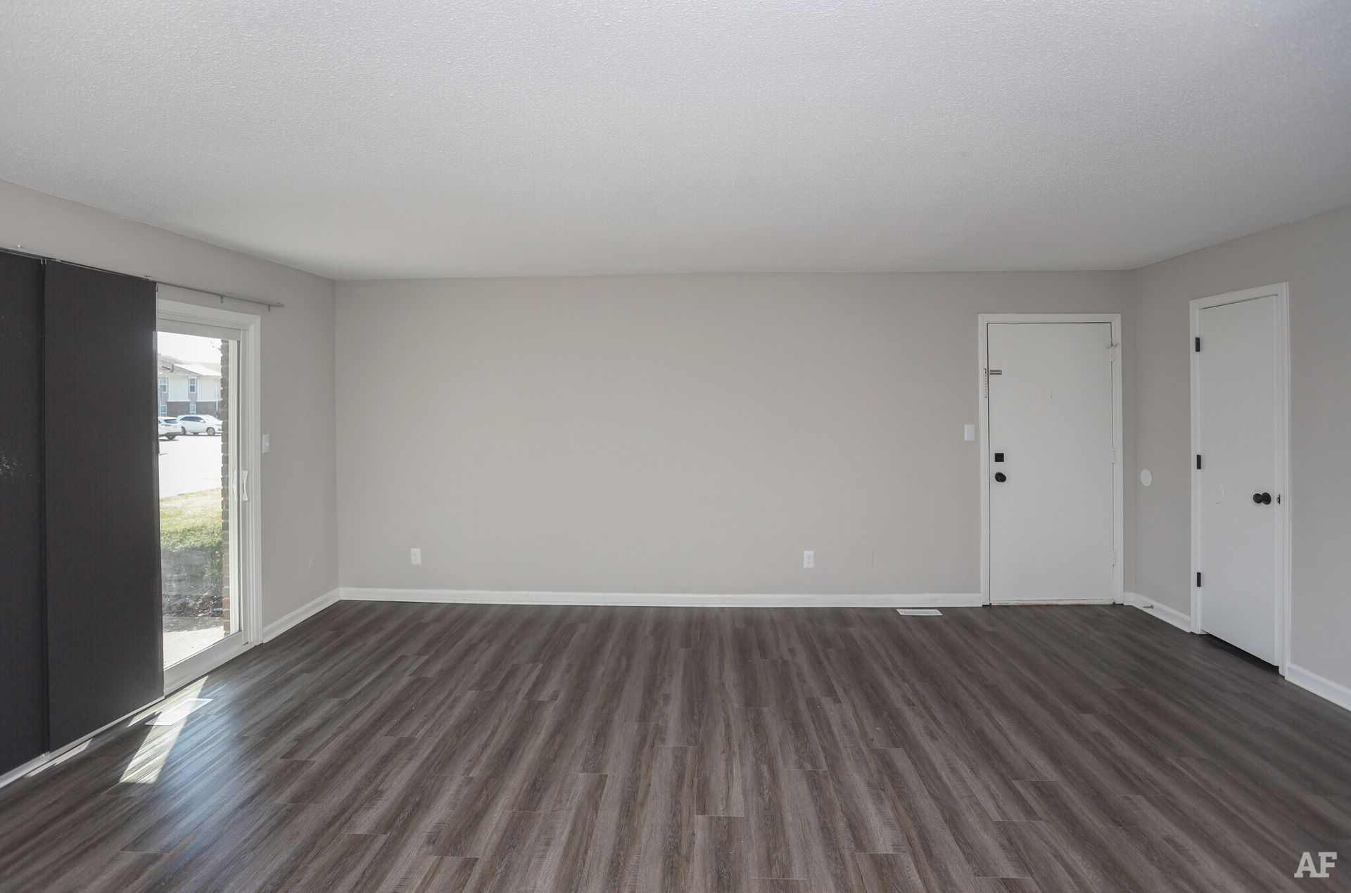 Empty living room with gray walls, wood-look flooring, and sliding glass door.