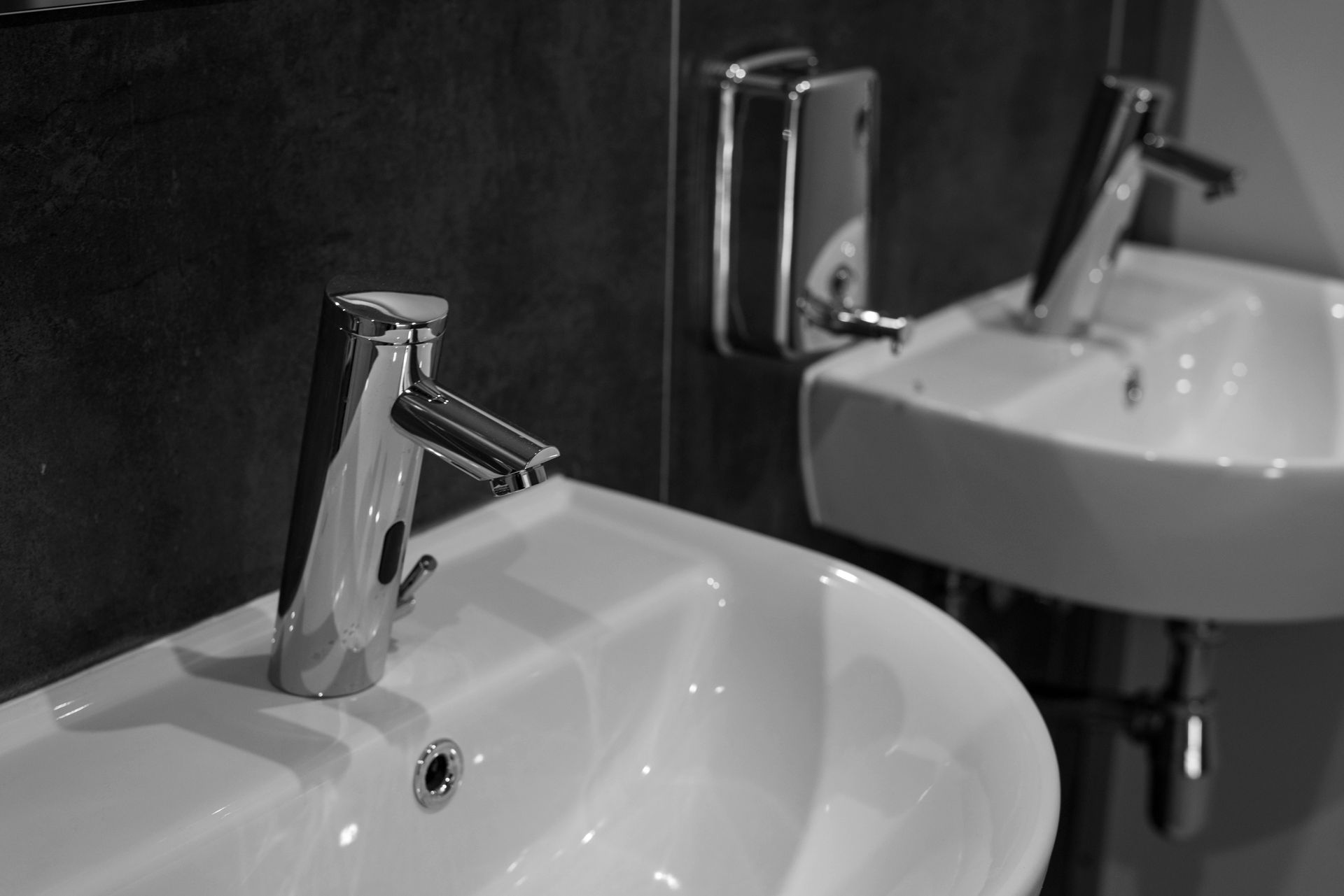 Two white sinks with chrome faucets against a dark wall, one with a soap dispenser above it.